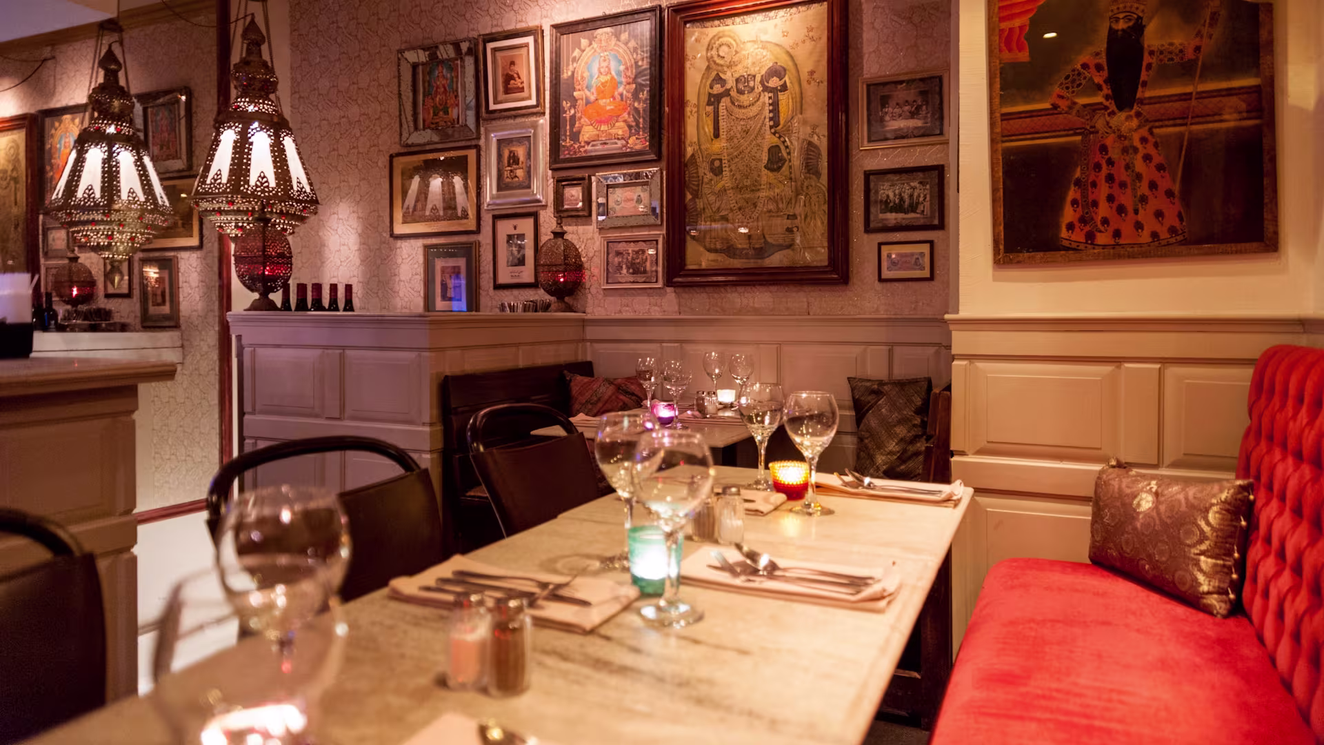Set tables, hanging lanterns, framed artwork and red upholstered seating inside Diwan in Stockholm